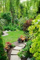 Jardin bien entretenu avec tremplins, pelouse, arbustes mixtes, bouleaux et pots avec hostas et heucheras