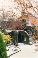 Jardin couvert de neige avec pergola d'if et pommes sauvages. The Crossing House, Shepreth, Cambridge