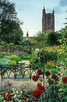 Vue sur jardin formel avec banc en fer forgé peint en bleu, vieux cadran solaire, chemins de gravier, roses, vivaces herbacées - Cerne Abbas, Dorset