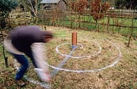 Homme traçant une spirale sur l'herbe rugueuse en automne avec un pot de peinture marqueur afin de planter une caractéristique de spirale de crocus pour le printemps