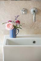Un arrangement de fleurs coupées dans une cruche à rayures bleues sur un évier de salle de bain
