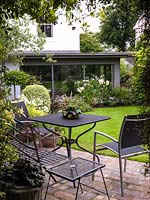 Vue de dessous de la pergola dans un petit jardin arrière avec une extension de cuisine moderne intégrée dans une banque de phormium, de palmier, d'alstroemeria et de lis.