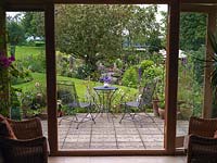 Les portes-fenêtres donnent sur la terrasse et le jardin de campagne au-delà avec des parterres de lys, de roses, de cosmos, de Verbena bonariensis, de lupin, d'allium, de buddleja et de vieux pommier.