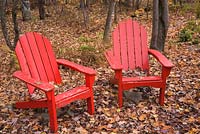 Deux vieilles chaises adirondacks en bois peint en rouge dans une forêt d'arbres à feuilles caduques d'Acer. Laurentides, Québec, Canada