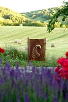 Panneau métallique rouillé orné de feuilles de fougère fournissant un point focal et un ancrage pour une clôture en fil de fer. Dans le paysage au Domaine de Cambou, Verfeil, Haute-Garonne, Midi Pyrénées, France.