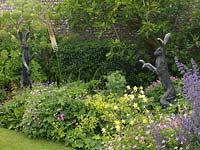 Sculptures de lièvre dans un parterre de fleurs d'été mixte