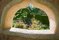 Pièce d'eau en métal conçue et réalisée par Michael Chaikin vue à travers une fenêtre dans le mur en torchis. Jardin planté de rodgersias, d'hamamélis, de roses et d'amsonia. Ferme Caervallack, St Martin, Helston, Cornwall, UK