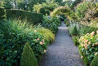 La longue marche avec des plates-bandes bordant des parterres contenant du phlox, des dahlias et des asters avec des arcs supportant des clématites. Wollerton Old Hall, nr Market Drayton, Shropshire, Royaume-Uni