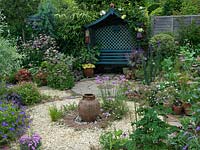 Un jardin et un patio en gravier sur le thème circulaire avec une plantation de style jardin de chalet. Le joystick Armeria et une urne en terre cuite constituent un point focal au centre du parterre de gravier.