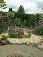 Un jardin et un patio en gravier sur le thème circulaire avec une plantation de style jardin de chalet. Le joystick Armeria et une urne en terre cuite constituent un point focal au centre du parterre de gravier.