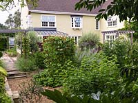 Vue de la maison et du jardin de 3 ans, plus de 9,5 mx 7 m de potager englouti avec 4 parterres de haricots verts avec des pois sucrés formés de cannes, de fraises et de légumes. Au-delà, terrasse, pergola.