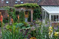 Derrière une ancienne remise des années 1850, un jardin de village avec des plates-bandes mixtes plantées de vivaces à floraison tardive.