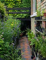 Carreaux d'argile à carreaux comme chemin à motifs dans un espace de jardin étroit, entre sous-sol de la maison et mur de soutènement. Pots de légumes et de fleurs.