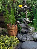 Totem de sculpture en bois flotté posé sur un parterre de vivaces d'été. Cache-pot en forme de tête inhabituelle remplie d'herbe tremblante.