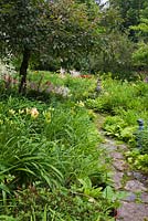 Chemin de dalle et parterres de fleurs avec Hemerocallis jaune - hémérocalle, fleurs roses Astilbe, Malus - pommetier et statuettes dans un jardin privé en été