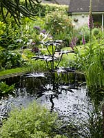 Au centre d'un étang circulaire, fontaine métallique sculptée en forme de gradins de feuilles d'où jaillit l'eau.