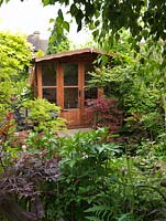 Summerhouse entrevu sur le feuillage, avec des pots d'acers - Acer japonicum King's Copse et A. palmatum.