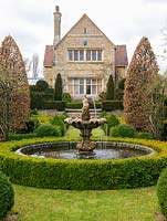 La maison victorienne donne sur un jardin à la française avec une piscine et une fontaine circulaires, des charmes, des topiaires d'ifs et des parterres d'or et des haies de boîtes sombres.