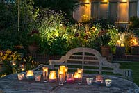 Une table avec des bougies et un parterre rétro-éclairé illuminent un jardin la nuit.