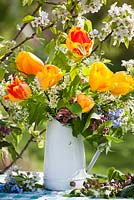 Affichage de fleurs de printemps dans une cruche. Tulipes jaunes, Prunus padus - cerisier des oiseaux, Myosotis arvensis, Allaria petriolata - moutarde à l'ail, Lamium orvala. Poirier en fleurs derrière - Pyrus 'Williams '.
