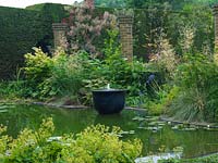 Jardin d'eau avec fontaine, jardin fleuri, pergola et pots. Piscine bordée d'alchémille, de sureau panaché, de rodgersia, d'acer, de Stipa gigantea, d'agapanthus, de smokebush.