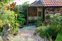 Un jardin de ville avec un coin salon couvert entouré de plantations tropicales de Canna, Musa et Trachycarpus.
