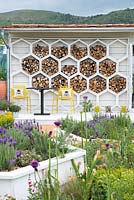 Mur de hangar couvert d'habitats d'insectes hexagonaux, table et chaises avec coussins d'abeille, parterres de fleurs hexagonaux surélevés avec Lavandula - The Bees Knees à l'appui de The Bumblebee Conservation Trust - RHS Malvern Spring Festival 2015