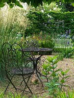 Jardin de gravier avec des meubles en métal vu à travers une haie de charme blanchie. Les vivaces comprennent Verbena bonariensis et Stipa gigantea.