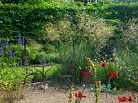 Un coin salon et un jardin de gravier planté de Crocosmia, Agastache, Gaura lindheimeri, Verbena bonariensis et Stipa gigantea 'Gold Fontaene '. Soutenu par une haie de charme blanchie.