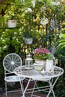 Espace détente sécurisé avec mobilier et rangements en métal. Affichage d'été avec Nemesia 'Bordeaux blanc' planté en pot d'ornement sur la table.