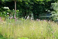 Squire's Garden Centres - Urban Oasis Petite prairie herbeuse non fauchée avec des fleurs sauvages soutenue par un parterre de fleurs vivaces et un hortensia 'Annabelle' avec table et chaises en métal. RHS Hampton Court Flower Show, 2015.