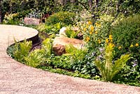 Chemin sinueux à travers un jardin planté d'arbres, d'arbustes, de fougères vivaces et de gros rochers de grès avec un ruisseau adjacent dans Vestra Wealth: Encore - A Music Lover's Garden at RHS Hampton Court Palace Flower Show 2015