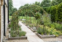 Parterres de plantes herbacées bordées de bois avec des obélisques en acier rouillé supportant des roses et des clématites.