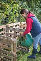 Femme ajoutant des déchets de jardin à un système de compostage à trois bacs construit à partir de palettes en bois recyclées