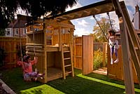 Filles sur balançoires dans un petit jardin urbain contemporain. Aire de jeux avec cadre d'escalade en bois. Jardin Ansari, Harrow