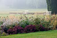 La pelouse principale avec des bancs et des ifs. Parterre de fleurs avec sedums et gaura linheimeri. Jardin de campagne. Été