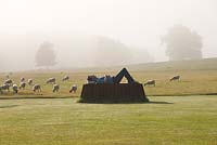 La pelouse principale en brume avec sculpture en bronze et acier corten par Sean Henry. Moutons paissant dans le champ au-delà.