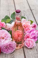 Eau de rose dans un vase en verre entouré de roses coupées