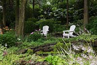 Deux chaises adirondacks en bois blanc sur le bord de l'étang avec des coussinets Nymphaea - Water Lily bordés de plantes Hosta à fleurs mauves, Québec, Canada.