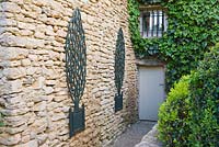 Jardin dans le Luberon, France, conçu par Michel Semini: arbres en bois trompe l ' oeil en pots sur le mur à côté de la porte arrière