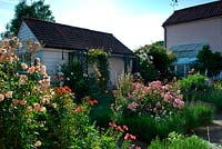 Vue sur le jardin de la cour fermée avec un aménagement paysager en dalles de pierre, des parterres d'îles de roses et de vivaces bordés de lavande et une tonnelle sur un bâtiment de jardin.