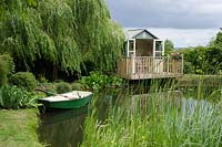 Pavillon à côté de Salix babylonica 'Pendula' donnant sur un étang avec un bateau