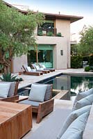 Vue sur la piscine moderne et la maison avec des chaises longues et un olivier mature au coucher du soleil.