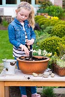 Jeune fille plantant un jardin alpin en pot. Ajoutez du gravier pour améliorer le drainage.
