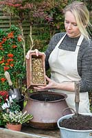 Planter un pot d'automne avec des fleurs blanches et des plantes à baies rouges. Étape 1, ajoutez du gravier au fond du pot en cuivre pour faciliter le drainage.