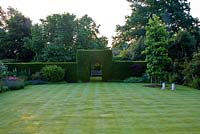 Pelouse rayée tôt le matin avec Taxus baccata - haie d'if et arcade. Morus nigra - Mûrier et siège en bois ornemental au-delà, Liquidamber et sièges sculptés à droite