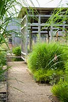 Au centre du jardin avant minimaliste, conçu par Christopher Bradley-Hole, se trouve un pavillon d'été contemporain en chêne vert entouré de hauts miscanthus, molinias et Macleaya microcarpa 'Spetchley Ruby '. Bury Court Barn, Bentley, Hants, UK