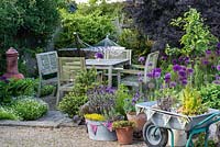 Un coin salon derrière un petit jardin en pot planté de lavande, d'origano, de thym, de sauge et de fraise dans des pots en terre cuite, une baignoire en métal et une brouette recyclée.