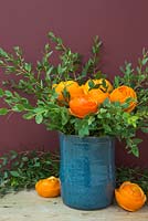 Têtes de fleurs en peau d'orange, accompagnées d'eucalyptus dans un vase bleu
