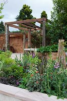 Parterre de jardin surélevé donnant sur une pergola en bois recyclé, salle à manger aux murs recouverts de bardeaux de cèdre.